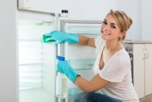 Happy Young Woman Cleaning Refrigerator At Home