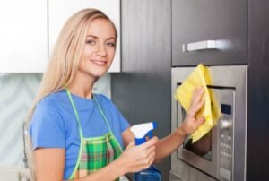 Woman Cleaning Microwave In Kitchen