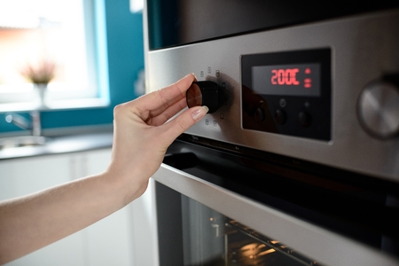 Woman's Hand Setting Temperature Control On Electric Oven