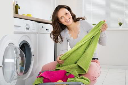 Young Happy Woman Folding Clothes Beside Dryer