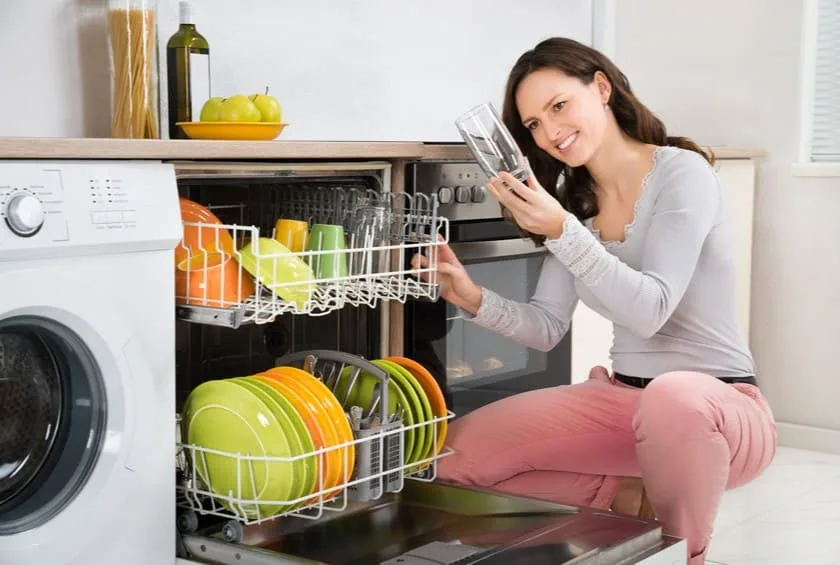 Young Woman Taking Glass From Dishwasher In Kitchen